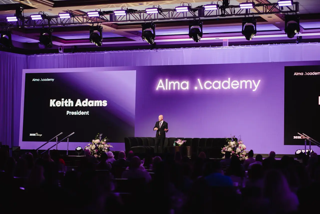 Alma Academy general session in a ballroom with a wide purple LED screen and a lighting truss overhead