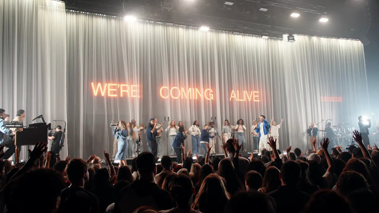WE'RE COMING ALIVE reads through the drape in red as the crowd lifts their hands
