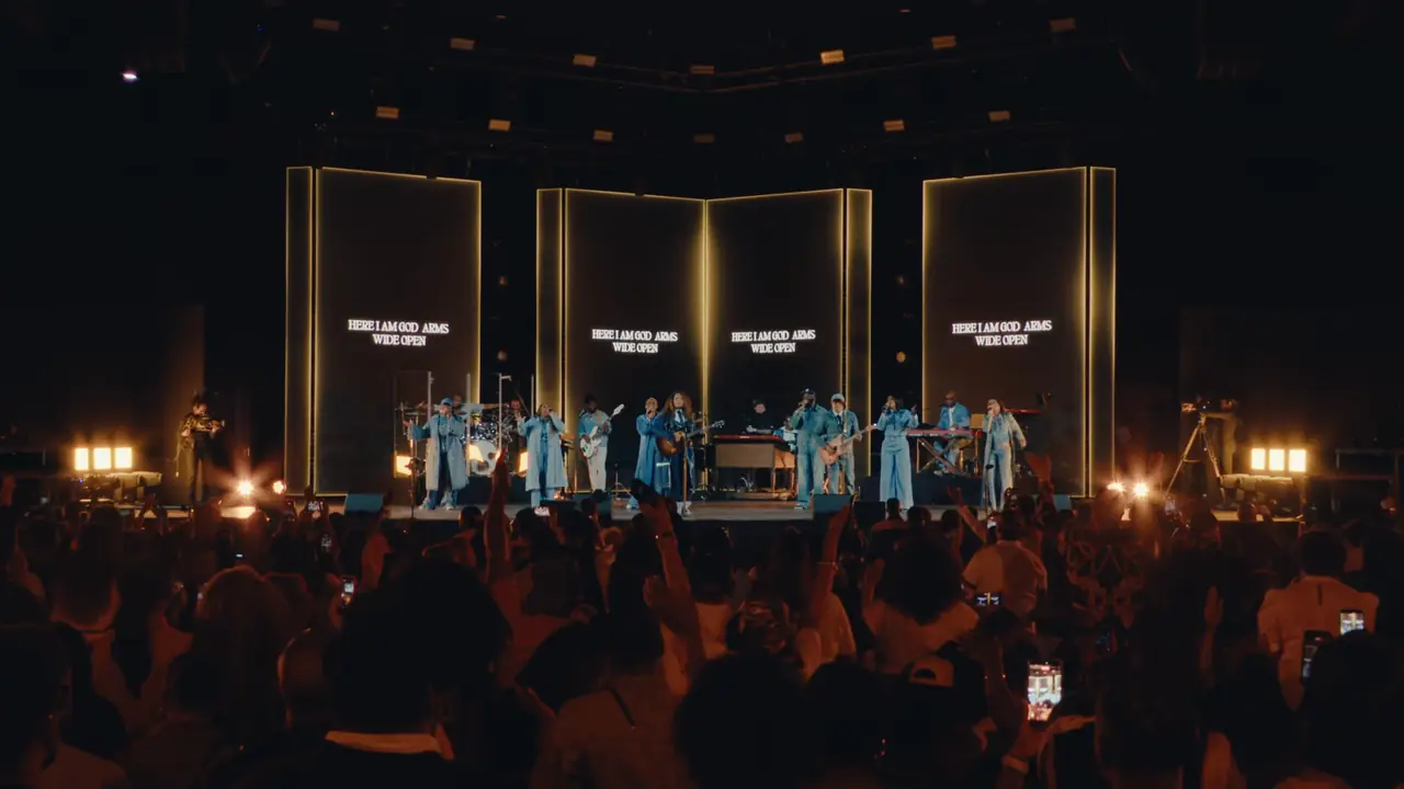 Tasha Unscripted live recording: wide view of the band and singers in front of three tall lit panels, warm light, crowd in the foreground