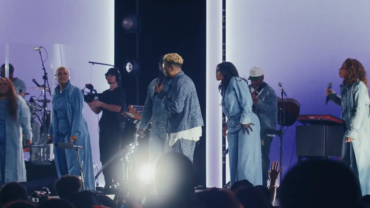Singers lined across the stage in front of the lavender-lit panels