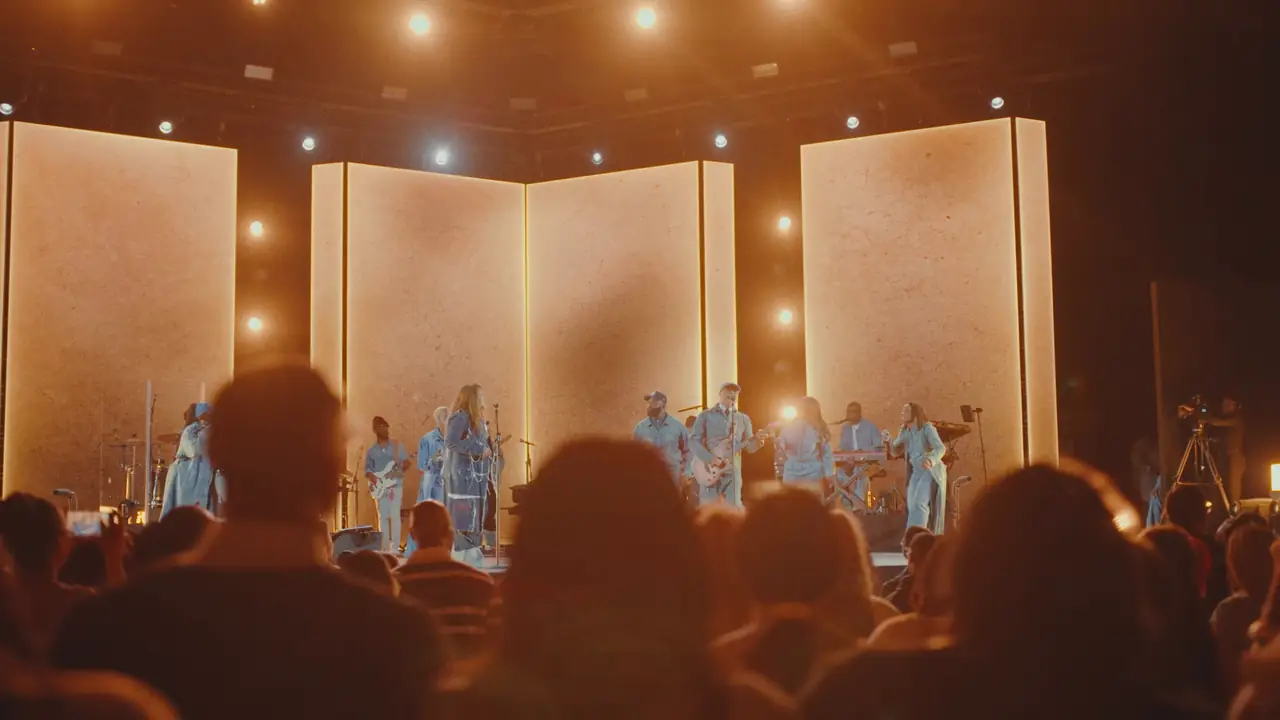 Hands raised in the crowd in front of the warm-lit panels and stage